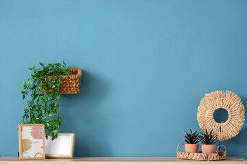 Wall Mural - Photo frames and wicker tray with houseplants on wooden chest of drawers near blue wall