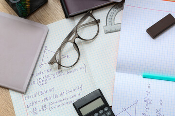 Wall Mural - Copybooks with math formulas, eyeglasses and stationery on wooden table, closeup