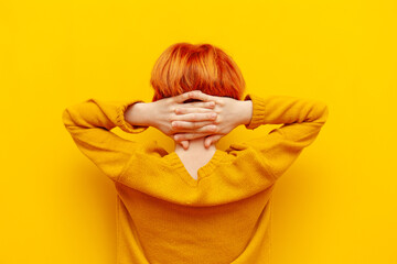 relaxed red-haired teenage boy holds his hands behind his head on a yellow isolated background, a child with an orange hairstyle rests and looks away, rear view