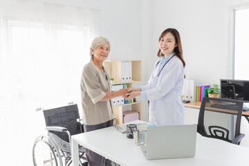 Asian female doctor warmly greeting elderly patient in medical office. They holding hand together, geriatric care, and positive doctor-patient relationship in a clinical setting.