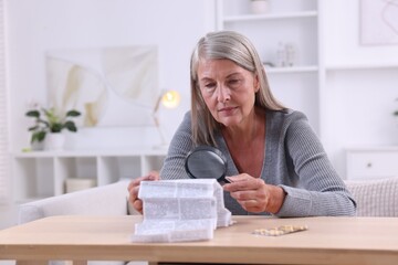 Sticker - Senior woman with magnifying glass reading medicine instruction at table indoors