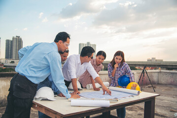 Civil construction engineer team meeting on construction site with teamwork wear safety suit trust team look at blue print on table consulting together safety hard hat construction engineer concept