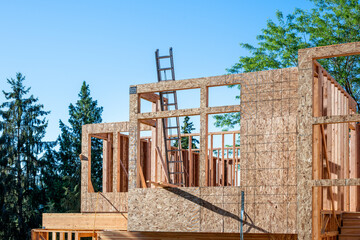 Summer construction season, new house build at the framing stage, aluminum extension ladder on 2nd floor leaning against exterior wall, early morning sunny day
