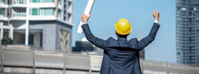 Banner construction engineer man hold blueprint wear blue shirt safety white hard hat at construction site industry plant. Panorama Architecture male civil engineer look at blueprint with copy space.