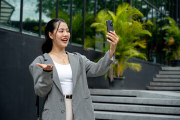 Asian businesswoman in a grey suit is waving her hand and talking on a video call on her smartphone