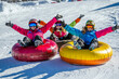 © Hanna - Three friends enjoy snow tubing on a winter day in a snowy landscape, wearing colorful outerwear and helmets