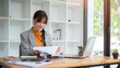 © bongkarn - A positive Asian businesswoman is reviewing the financial report while working at her desk.