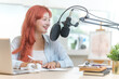 © wattana - Pretty young woman speaking into professional microphone mounted, recording a podcast  in her studio.