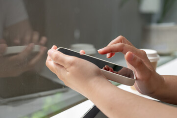 Wall Mural - A close-up side view image of a woman using her smartphone while sitting in a coffee shop.