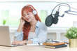 © wattana - Smiling young woman wearing headphones and speaking into a professional microphone, recording podcast or content for blog.