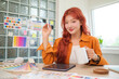 © wattana - Female graphic designer using a digital tablet at creative workspace surrounded by various colour swatches and design charts.