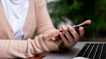 Wall Mural - A close-up image of a woman is using her smartphone while working remotely at a table in a garden.