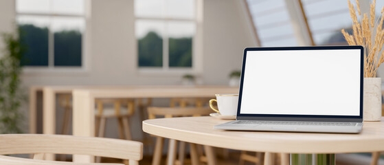 Poster - A laptop computer on a wooden table in a contemporary, minimalist co-working space.