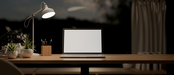 Wall Mural - A laptop mockup on a table in a modern dark room at night, illuminated by a table lamp.