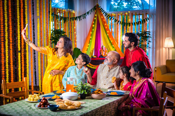 Portrait of happy Indian family in traditional outfit celebrating Diwali together at home eating food.