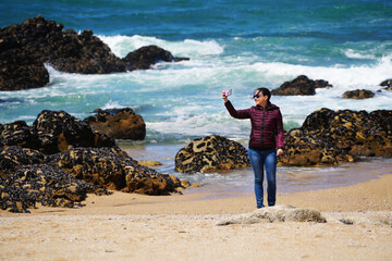 A young woman enjoys an empty beautiful beach with sand and blue sky in Porto, Portugal.