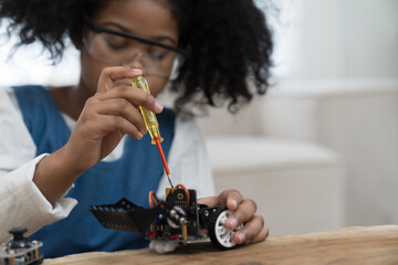 Girl student learning and building project toy robotics technology at home. African American child girl training and control toy robot in classroom