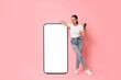 © New Africa - Beautiful young woman with smartphone standing near big mobile phone with blank screen on pink background