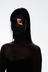 Brunette girl posing in a beam of light in the studio, light and darkness.