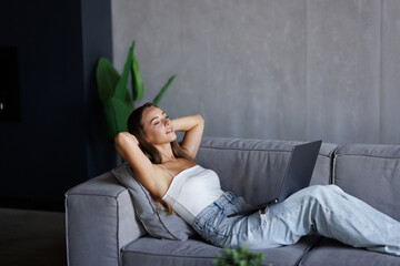 Beautiful young relaxed woman resting while sitting with laptop on sofa at living room