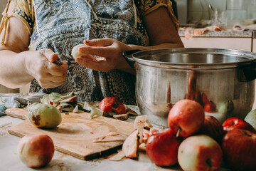 Old woman cuts apples for jam. Red ripe apples on the table next to the jam pot. An elderly woman makes jam in her cottage on a farm. Conservation and harvesting. Homemade delicious food