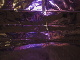 Wall Mural - purple light reflects on silver plastic sheet for abstract dark background.