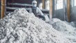 © VK Studio - A pile of white powder sits in a factory, with a worker in protective gear standing in the background, highlighting industrial processes and safety.