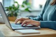 © 为轩 张 - Close-up of a woman typing on a laptop in an office, focus on hands and screen with a blurry background, wearing a blue sweater, wooden desk with a notebook, modern interior design.