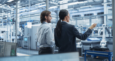 Leinwandbilder - Young Caucasian Engineer and Asian Technician Having Conversation and Using a Laptop Computer. Specialists Monitoring, Analyzing Conditions at a Modern Electronics Factory with Automated Conveyor