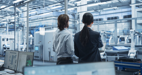 Leinwandbilder - Young Caucasian Engineer and Asian Technician Having a Conversation and Using a Laptop Computer. Specialists Monitoring, Analyzing Conditions at a Modern Electronics Factory with Automated Conveyor