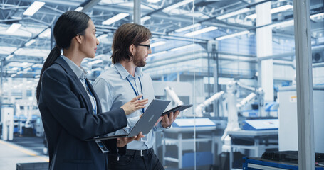 Fototapete - Portrait of Cheerful Engineer and Happy Asian Scientist Using Laptop and Tablet Computers, Talking in a Factory Facility with Robots Producing Modern Electronic Components for Different Industries