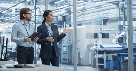 Fototapete - Two Diverse Engineers Walking in Office, Using Tablet Computer at an Electronics Factory. Female and Male Specialists Chatting, Monitoring Robots on a Modern Assembly Line