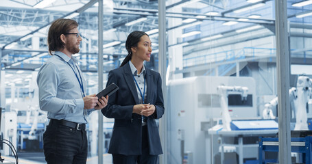 Fototapete - Two Diverse Engineers Walking in Office, Using Tablet Computer at an Electronics Factory. Female and Male Specialists Chatting, Monitoring Robots on Modern Assembly Line.