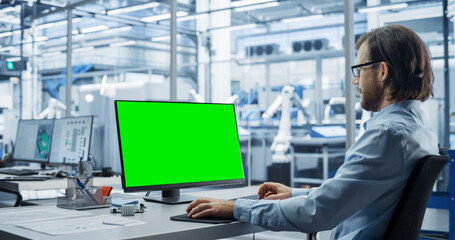 Fototapete - Robotics Engineer Working on a Desktop Computer with Green Screen Chromakey Mock Up Display in a Factory Office. Technological Research and Development Facility with Autonomous Assembly Conveyor