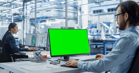 Leinwandbilder - Robotics Engineer Working on a Desktop Computer with Green Screen Chromakey Mock Up Display in a Factory Office. Technological Research and Development Facility with Autonomous Assembly Conveyor