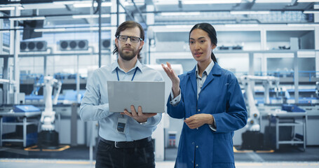 Leinwandbilder - Caucasian Man and Asian Female Having a Conversation at Industrial Facility. Advanced Factory Employees Working Together, Using Laptop Computer for Supervising Work Process in a Modern Facility