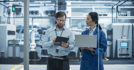 Leinwandbilder - Caucasian Engineer and Asian Female Project Manager Standing in Office, Talking, Using Computers and Monitoring Production at a Modern Automated Electronics Manufacture with AI Robotic Arms