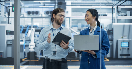 Leinwandbilder - Caucasian Engineer and Asian Female Project Manager Standing in Office, Talking and Using Computers and Monitoring Production at a Modern Automated Electronics Manufacture with AI Robotic Arms