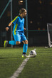 © PoppyPix - vertical shot of a blonde girl in a blue uniform kicking a ball while practicing at night. High quality photo