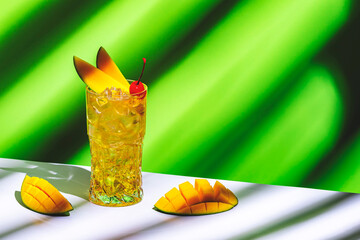 Wall Mural - Mango and rum alcoholic cocktail drink with syrup, ginger beer, lemon juice and ice. Green background, hard light