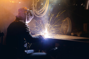 man in a welding mask welds a pipe in a dark workshop. welding smoke in the face, close-up