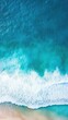 © Exnoi - An aerial view of a serene ocean scene with gentle waves rolling towards the shore, the water transitioning from deep blue to light green near the coast