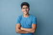 © IQRAMULSHANTO - Young Hispanic man in blue t-shirt, arms crossed, smiling at camera, isolated blue background.