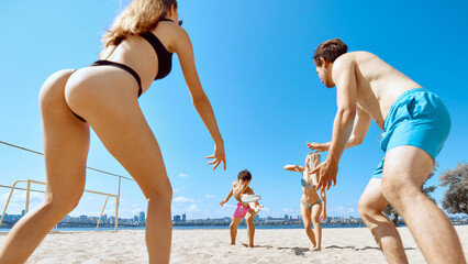 Active summer vacation. Young people, friends playing frisbee in beach by the river, enjoying dynamic game and good company. Concept of sport, summer activity, leisure games, friendship