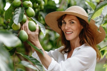 Canvas Print - A pretty woman in a hat smiles while harvesting fresh fruit in a lush orchard outdoors.