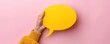 © Nanda - Hand holding a yellow speech bubble against a pink background. Concept of communication, conversation, and ideas.