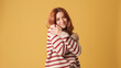 © Andrii Nekrasov - Cute red-haired woman dressed in sweater hugs herself looking at camera on yellow background. Beautiful girl poses in studio with blank space on yellow wall for your promotion