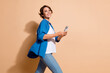© deagreez - Photo of cheerful young hr manager lady in smart casual outfit use smartphone when strolling at office isolated on beige color background