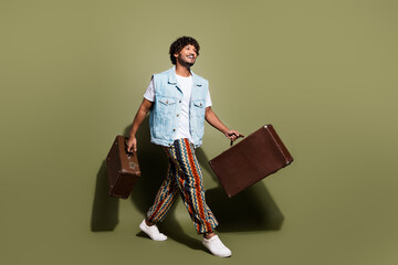 Poster - Full size photo of handsome young guy walk carry retro valise wear trendy jeans outfit isolated on khaki color background