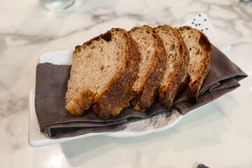 close up of four pieces of sliced wheat grain Sourdough gluten Bread on a grey tissue on a white plate in a marble pattern table